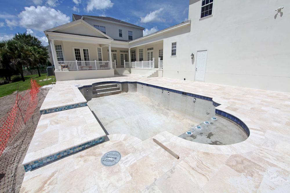 Custom residential pool under construction with spa and travertine deck, showing how long does it take to build a pool in Florida