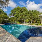 Custom pool designs featuring a modern backyard swimming pool with an attached spa, stone decking, and tropical landscaping.