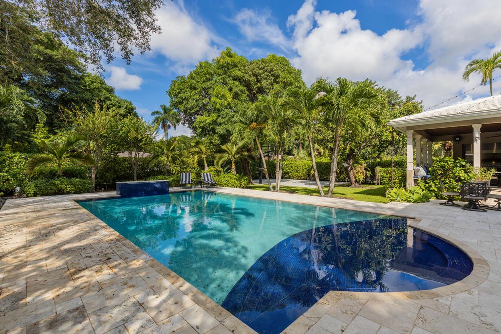 Custom pool designs featuring a modern backyard swimming pool with an attached spa, stone decking, and tropical landscaping.